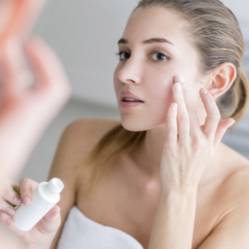 young woman applying cream on her face